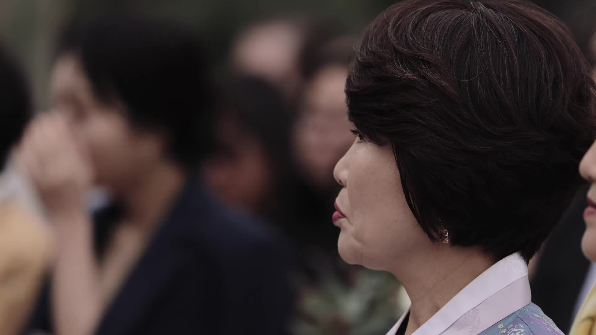 Profile of a guest in pale blue hanbok with white collar watching Manny and Jasmine's Korean wedding ceremony