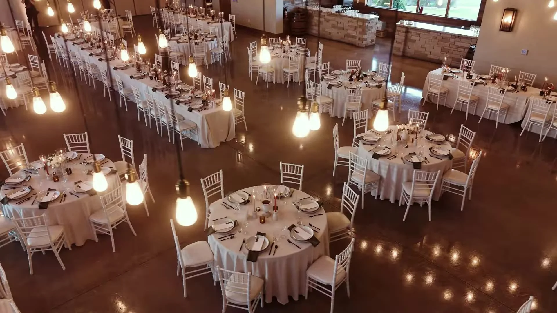 Empty reception hall at Canyonwood Ridge in Dripping Springs, Texas, with Edison bulbs and white tables