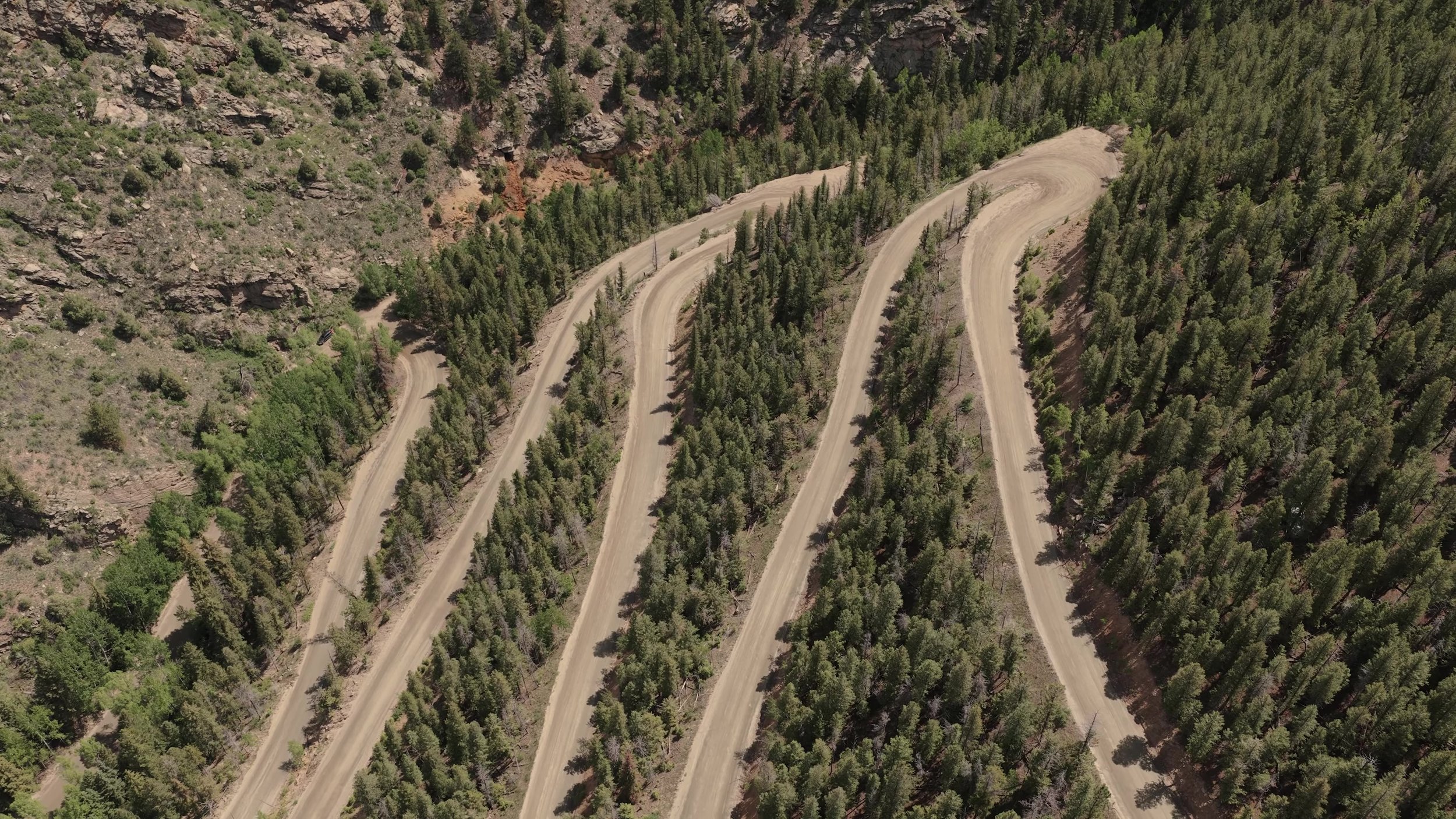 Aerial view of dirt switchbacks through pine forest on the mountain road to Northstar Gatherings near Idaho Springs, Colorado