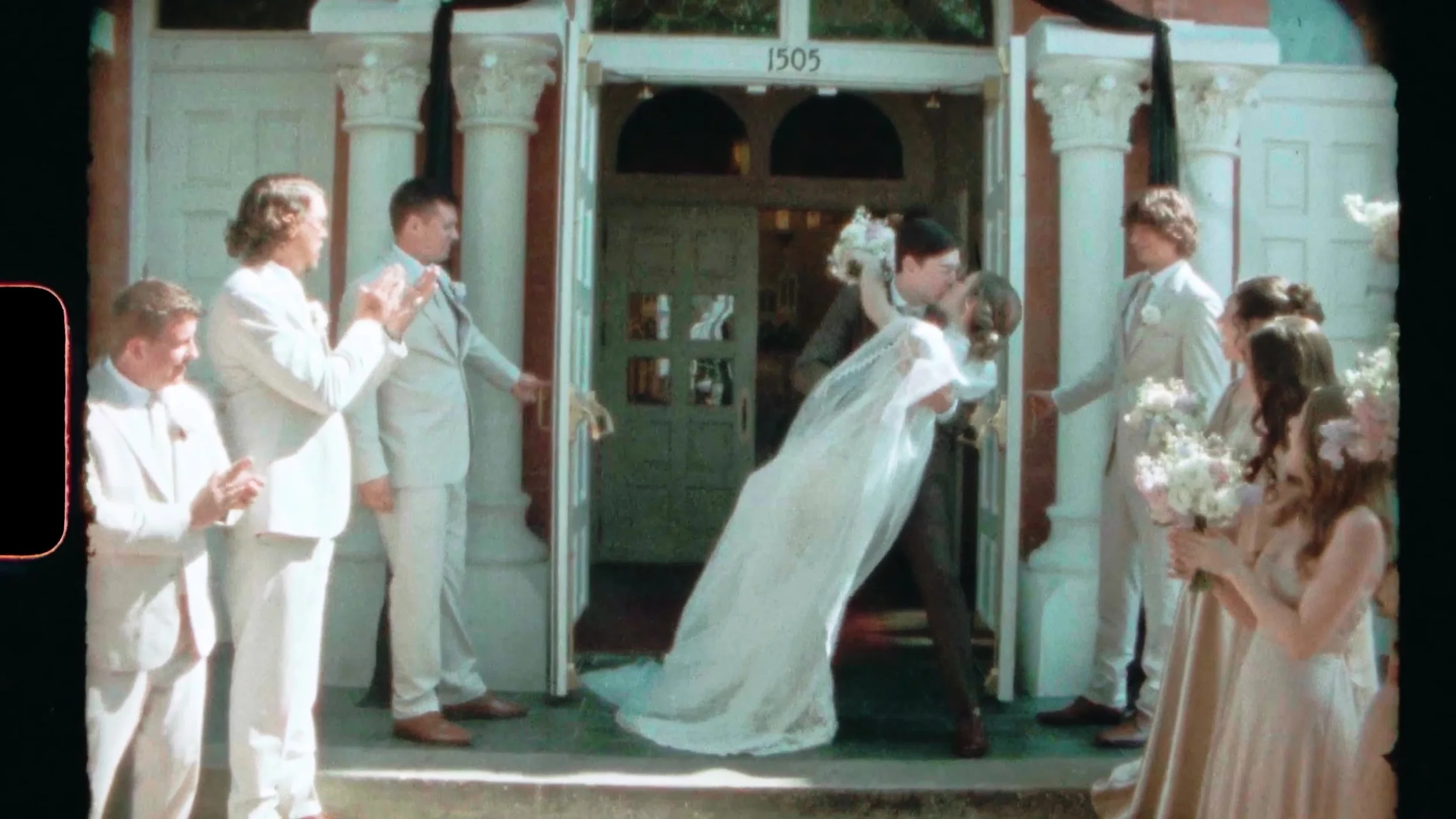 Bride and groom dip kiss at white doors with wedding party clapping outside a Houston church on film