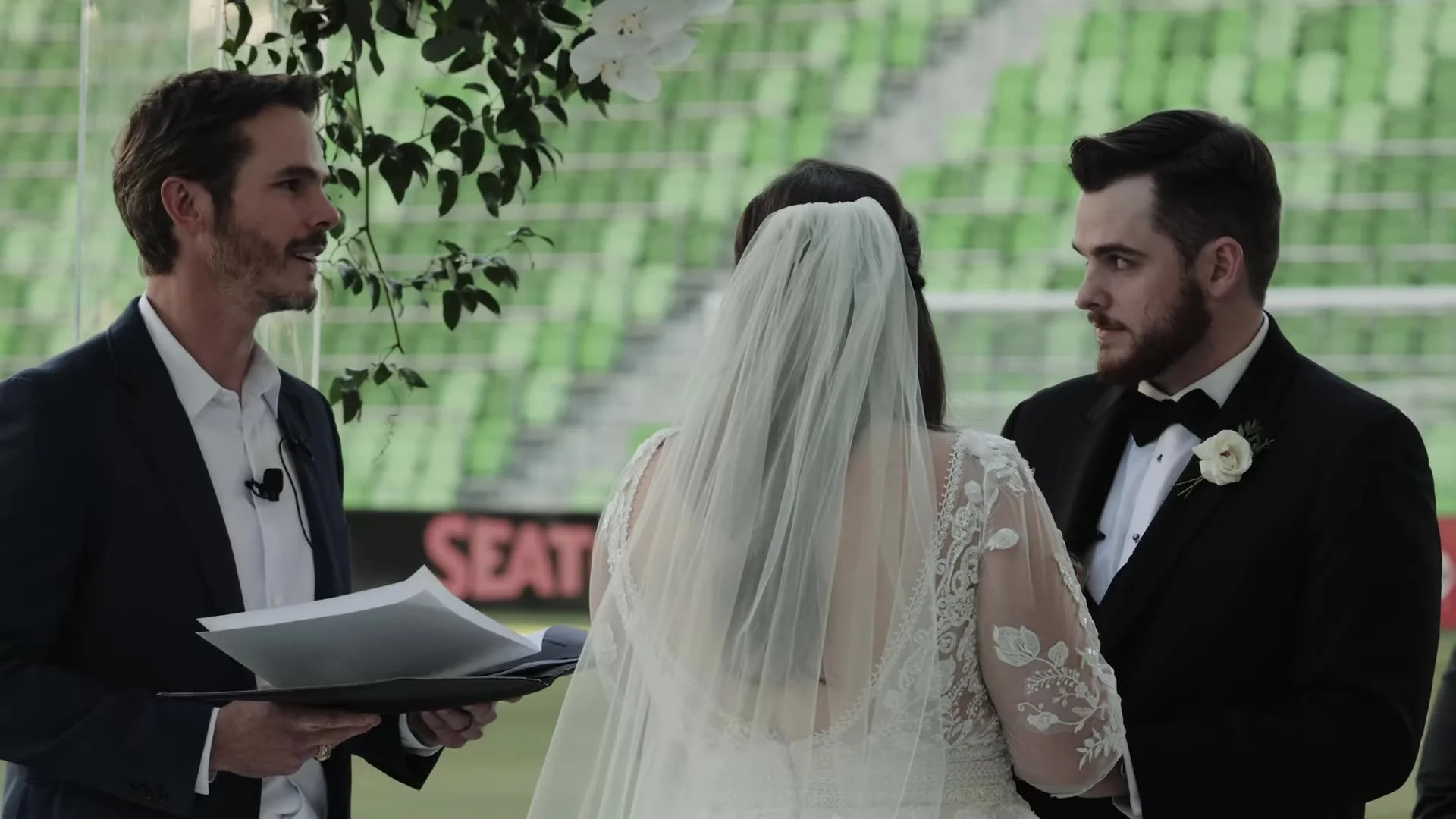 Gabby and Nic with their officiant during vows against green seats at Q2 Stadium in Austin, Texas