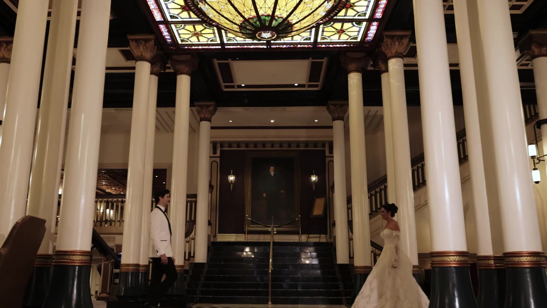 High angle of Grant and Anna between columns and the staircase under The Driskill stained glass dome in Austin