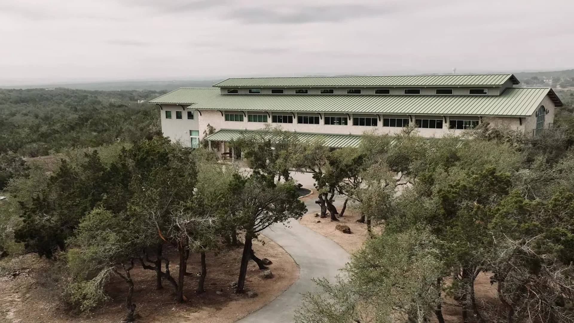 Wide landscape of The Terrace Club venue with green roof among Texas Hill Country trees near Austin