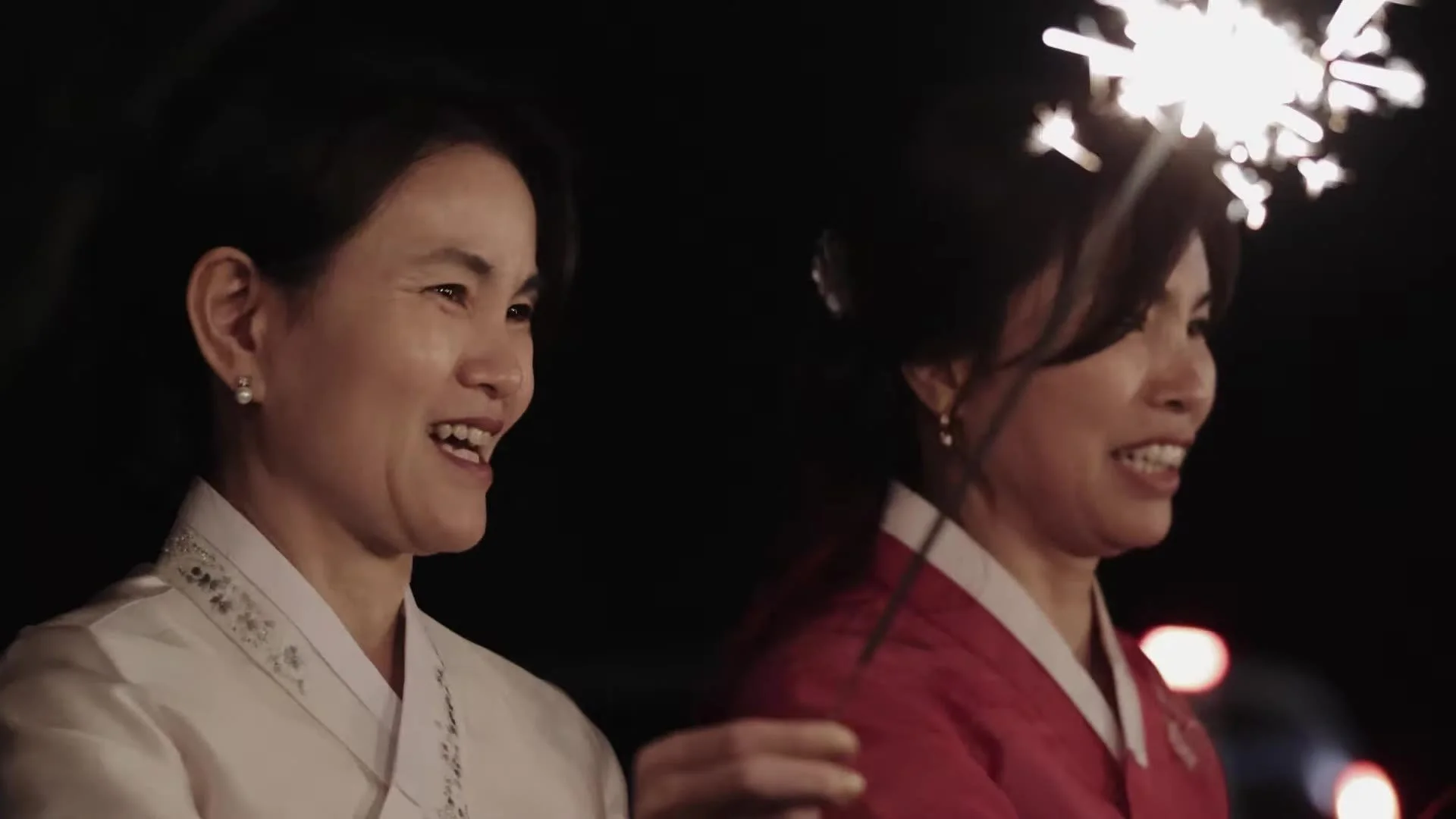 Two women in Korean hanbok smiling at night with a wedding sparkler at The Terrace Club Austin