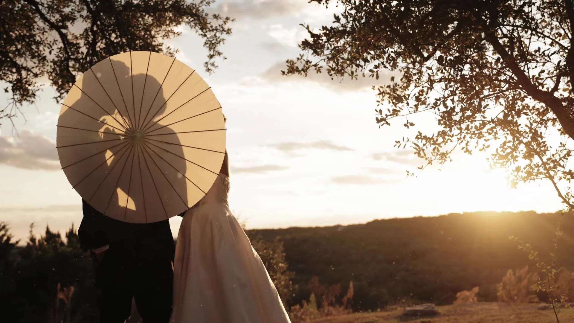 Jason and Rachel under a parasol at sunset among oaks at Canyonwood Ridge in the Austin Hill Country
