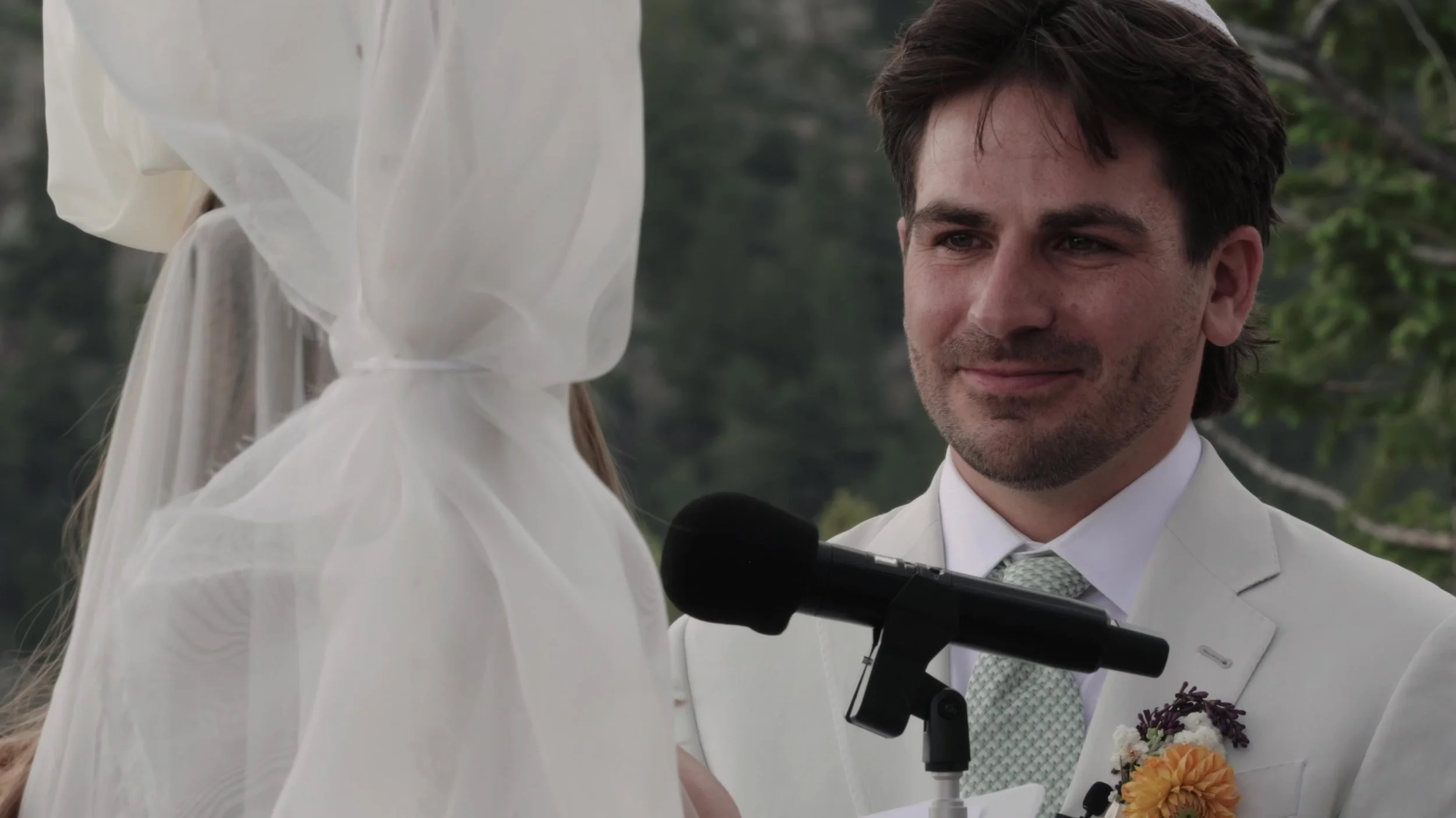Groom in a cream suit and kippah smiling during the ceremony at Northstar Gatherings in Idaho Springs, Colorado