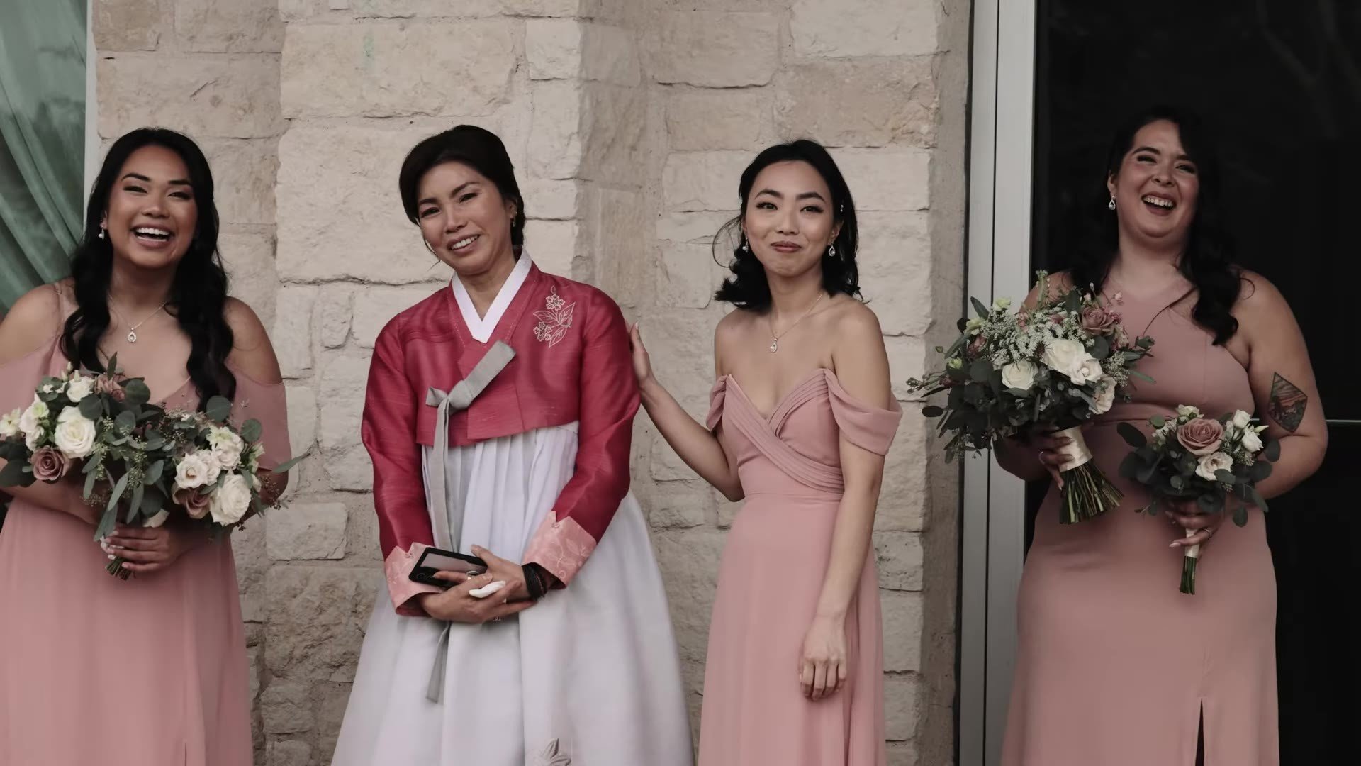 Woman in magenta and white hanbok with bridesmaids in dusty rose against a stone wall at The Terrace Club