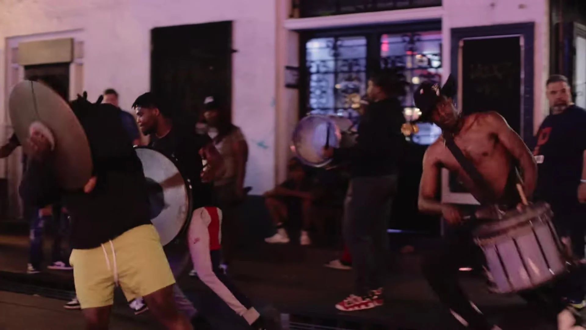 Street percussionists with drums and metal lids on a French Quarter sidewalk at night in New Orleans