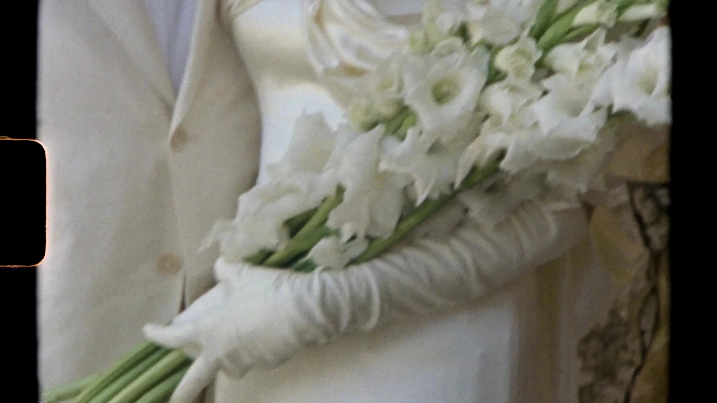 Sarah's white gloved hands holding a long stem white bouquet in Super 8 grain at Camp Lucy Vineyards