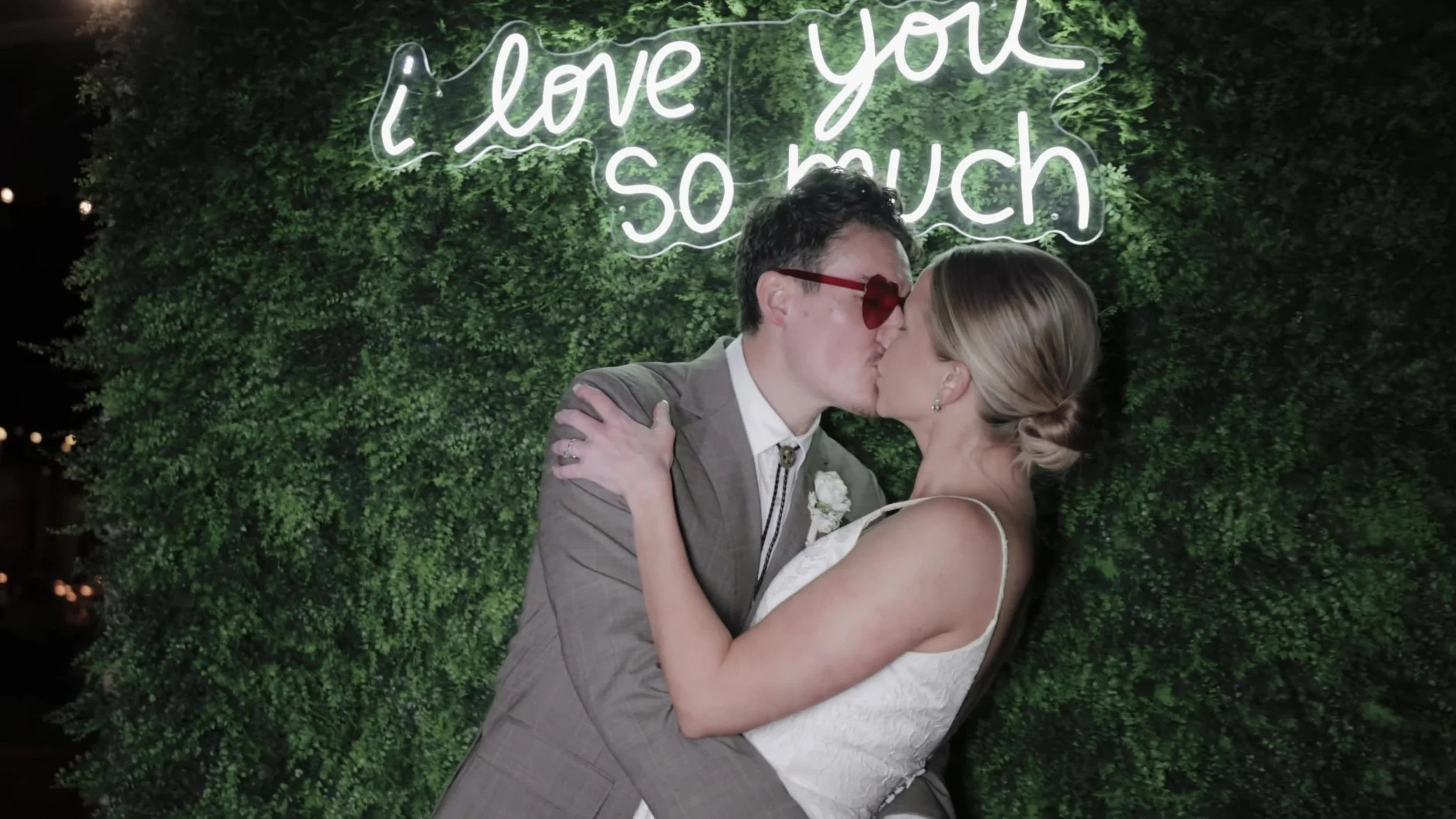 Heather and Chris kissing in front of an I love you so much neon sign at Lady Bird Johnson Wildflower Center in Austin, Texas