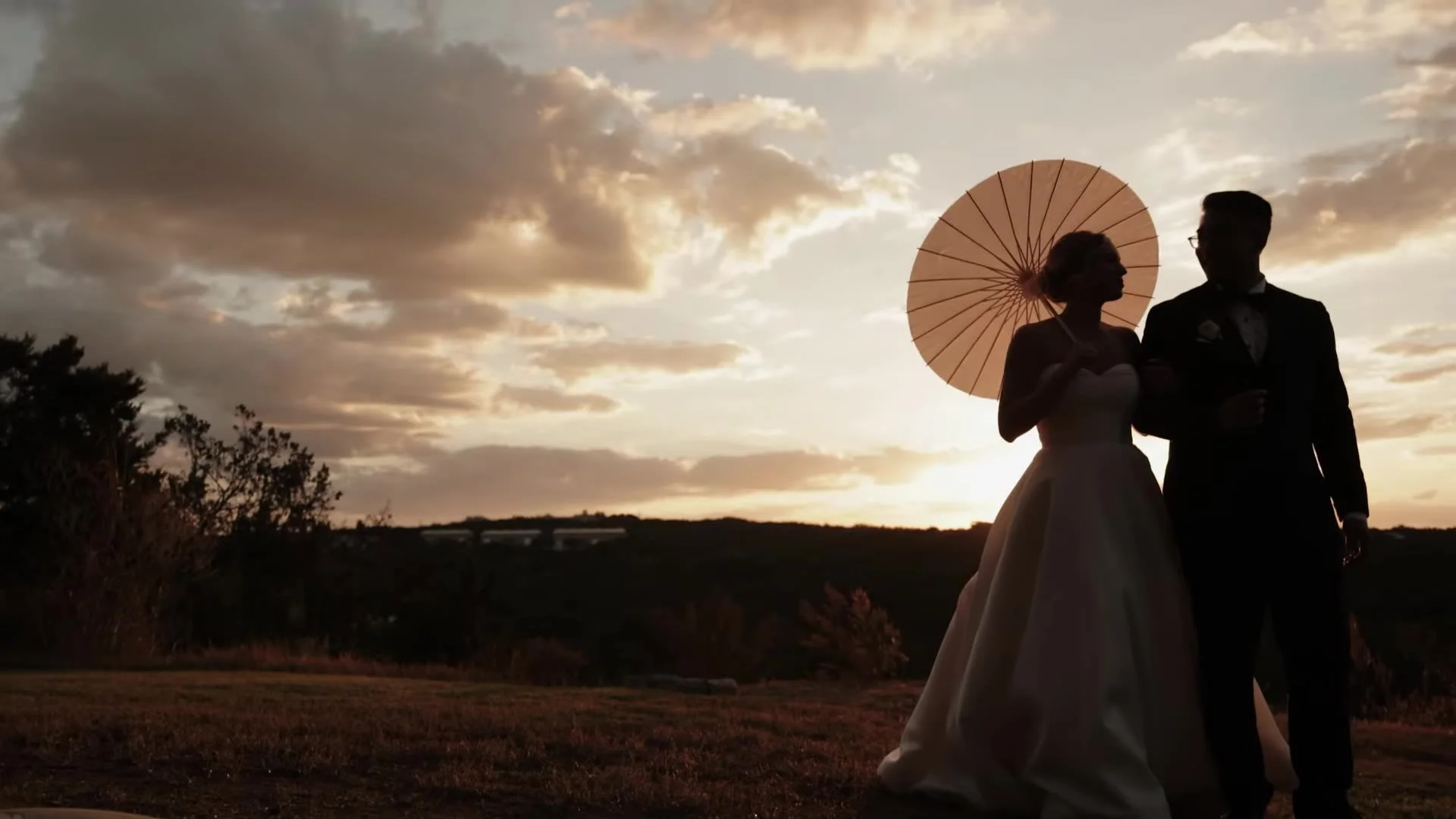 Wide sunset silhouette of Jason and Rachel with a parasol at Canyonwood Ridge in the Austin Hill Country, Texas