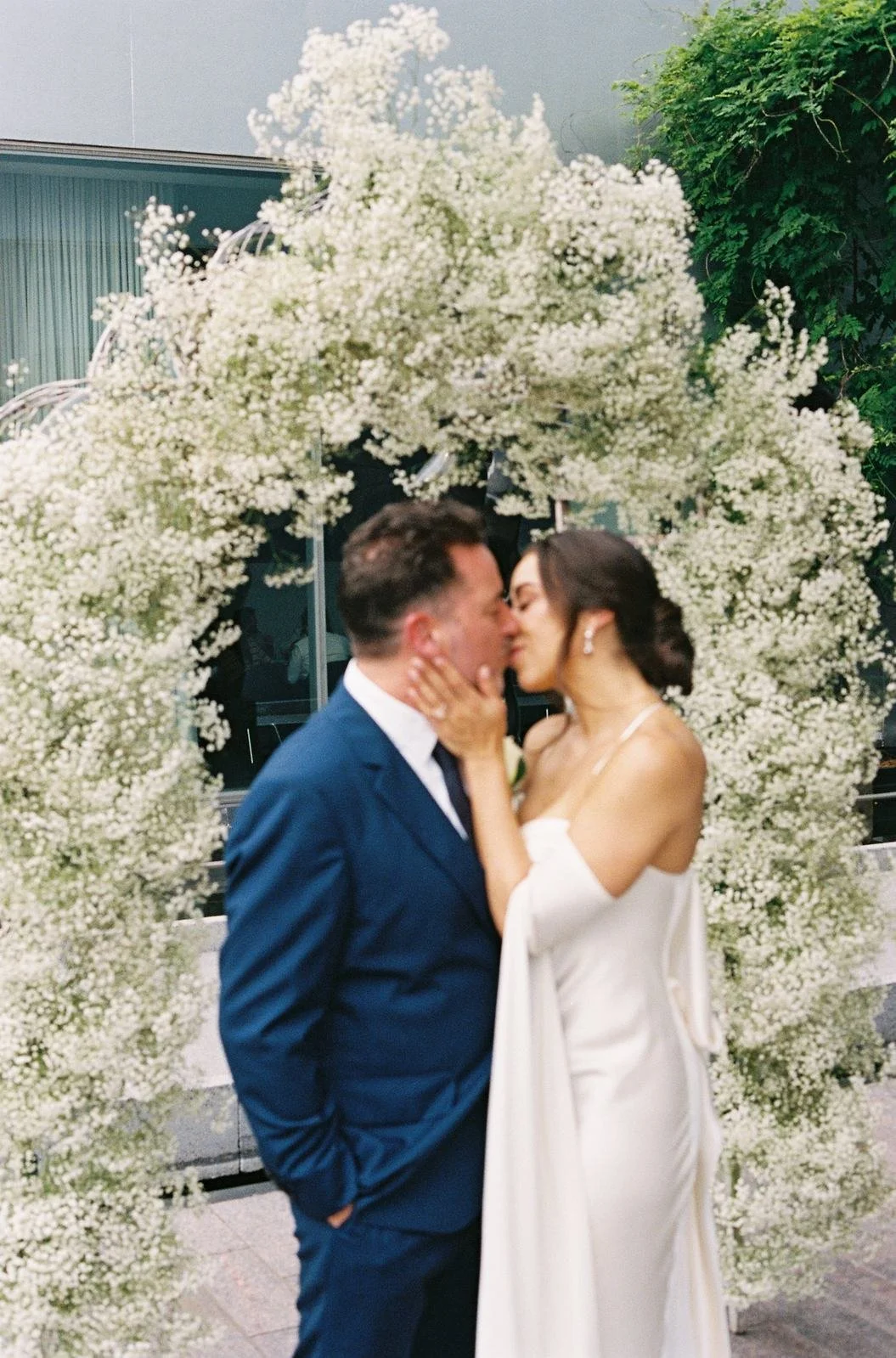 Bride and groom kissing under a baby's breath floral arch