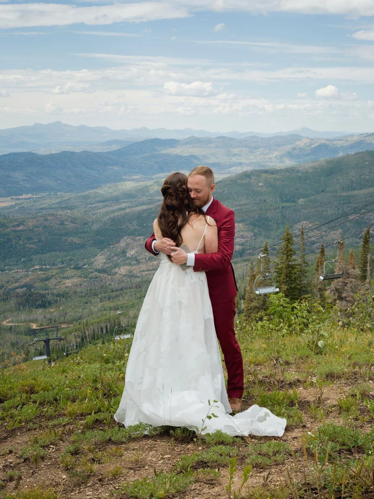 Bride and groom embracing on a mountain ridge overlooking a ski resort