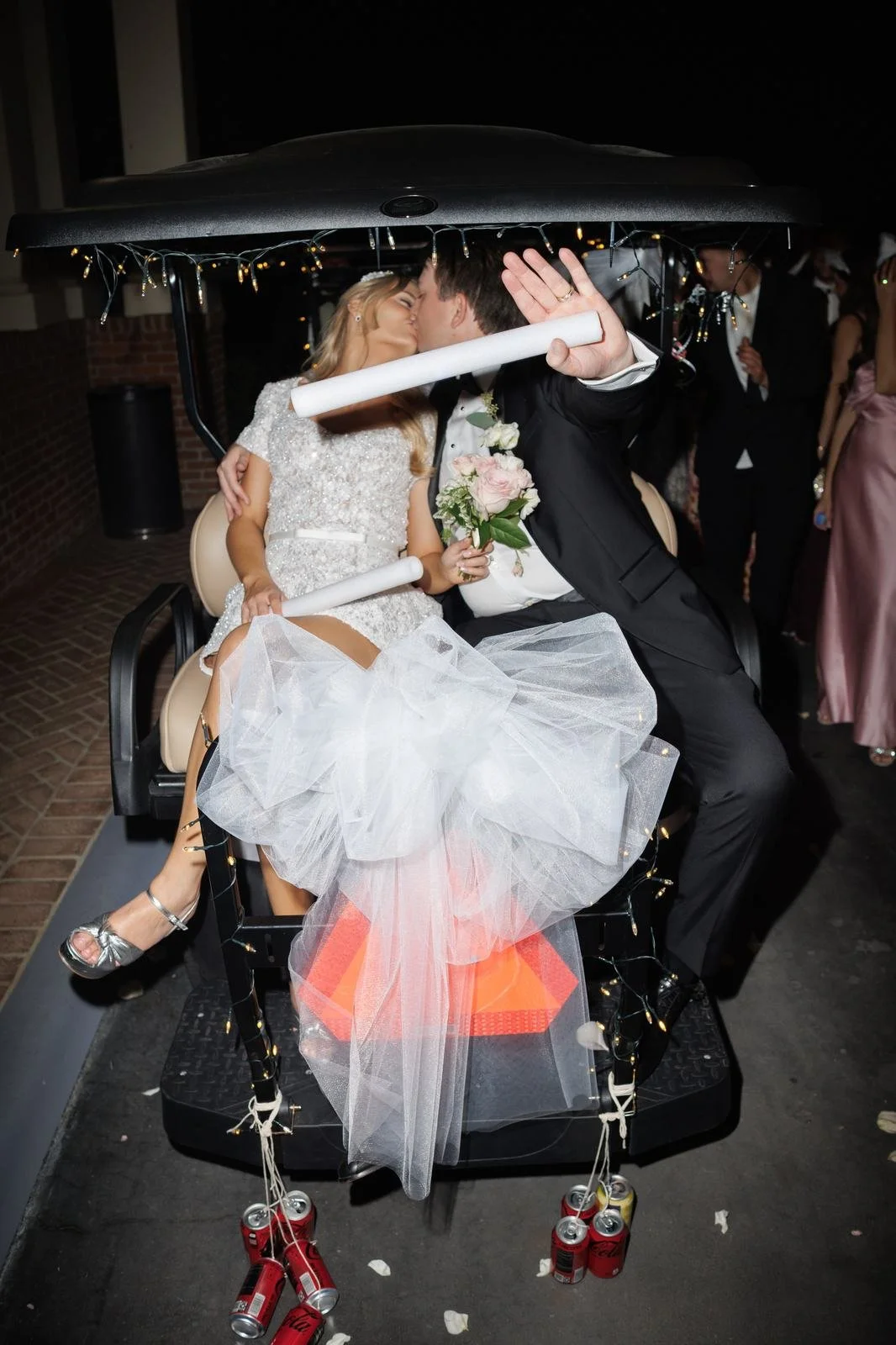 Bride and groom kissing on a golf cart decorated with string lights