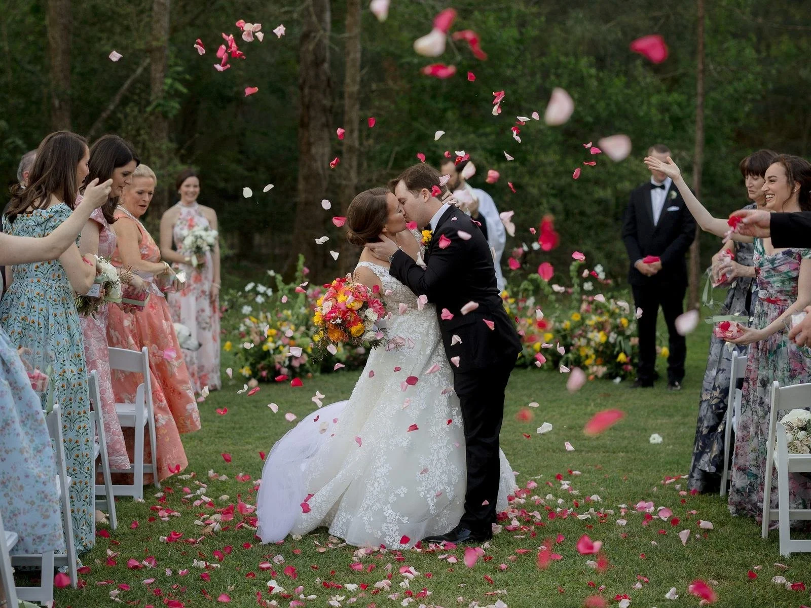 Bride and groom kissing as guests throw flower petals