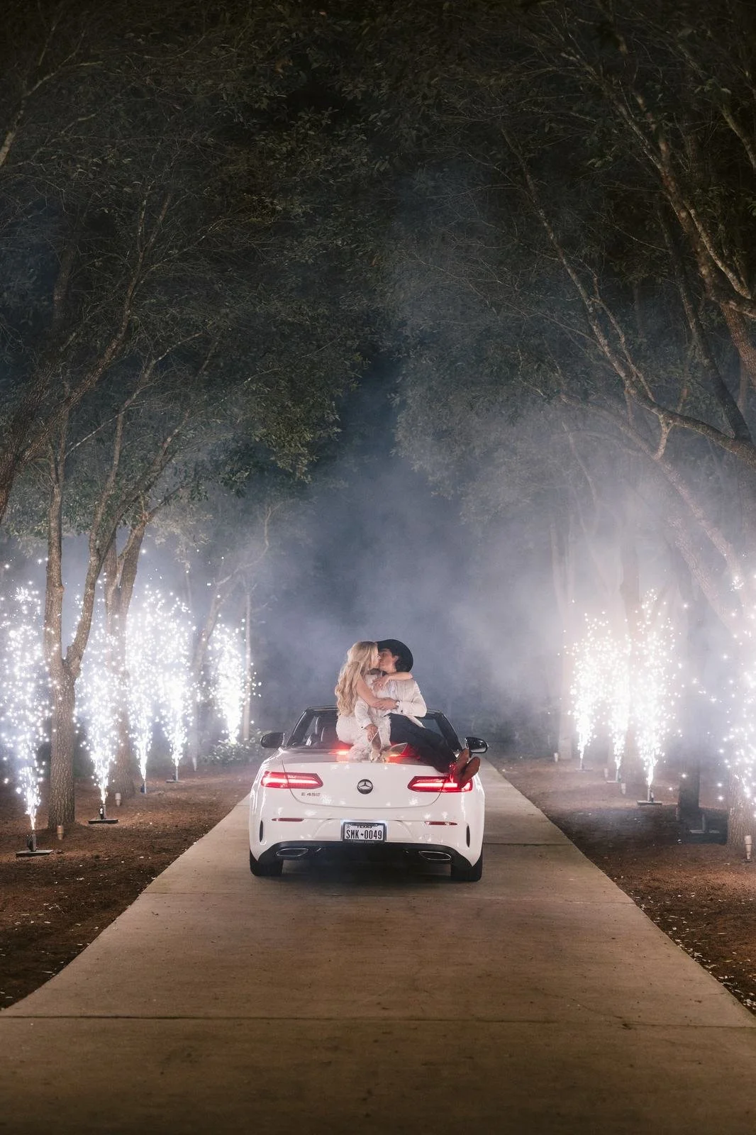 Bride and groom on the back of a car amid sparkler smoke at night