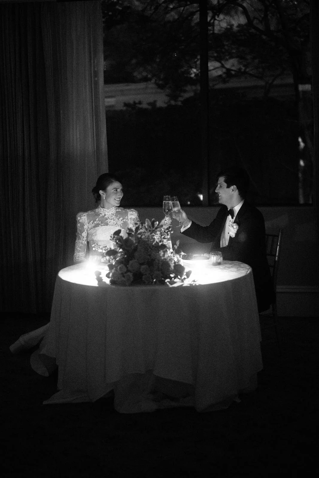 Black and white photo of bride and groom toasting champagne at a candlelit sweetheart table