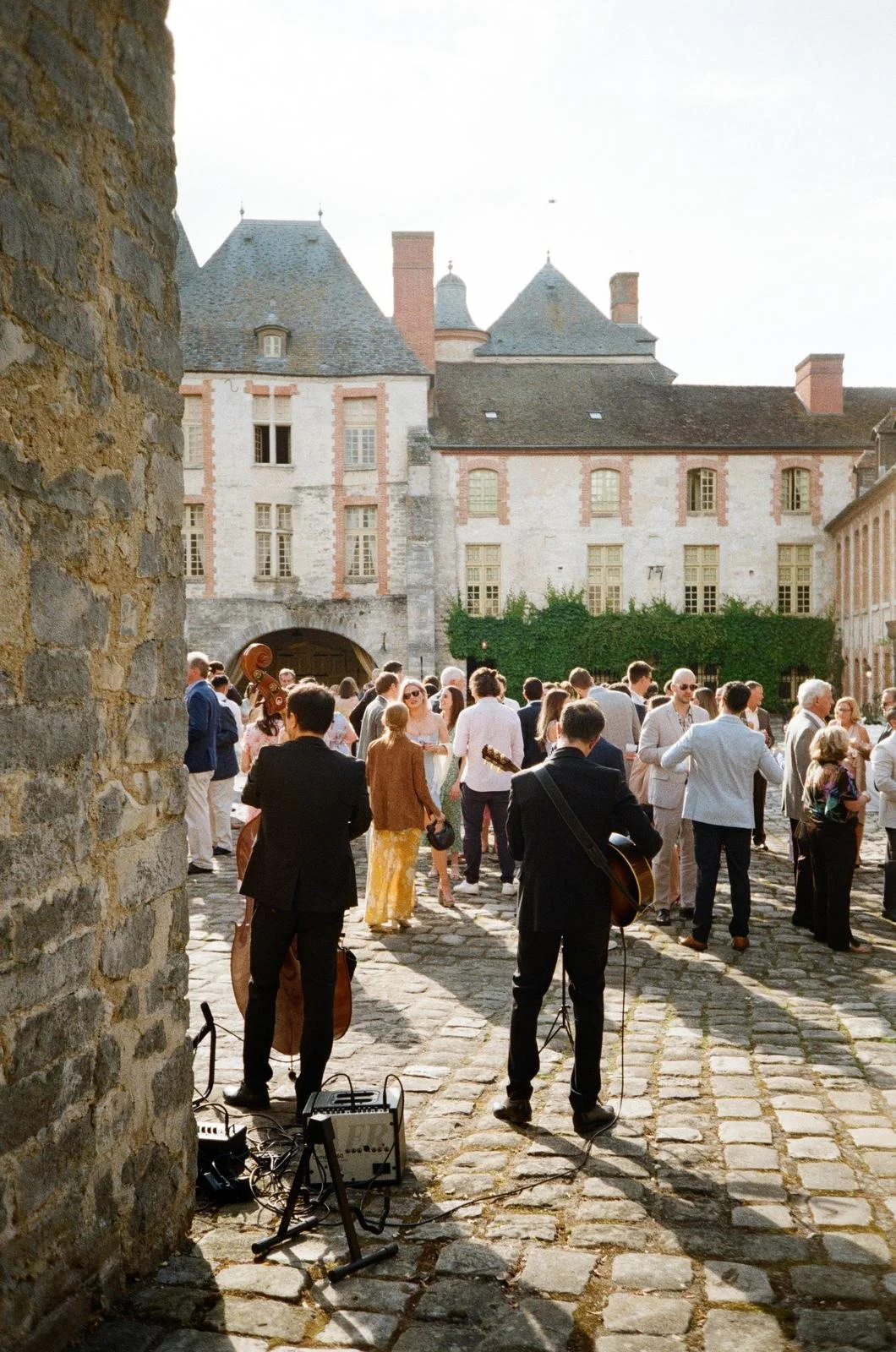 Wedding guests gathered in a stone courtyard of a French chateau with live musicians
