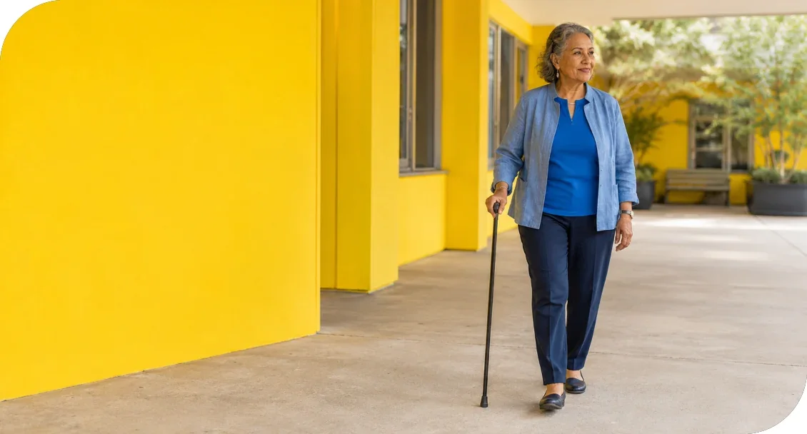 An older woman walking with a cane along a covered outdoor walkway.