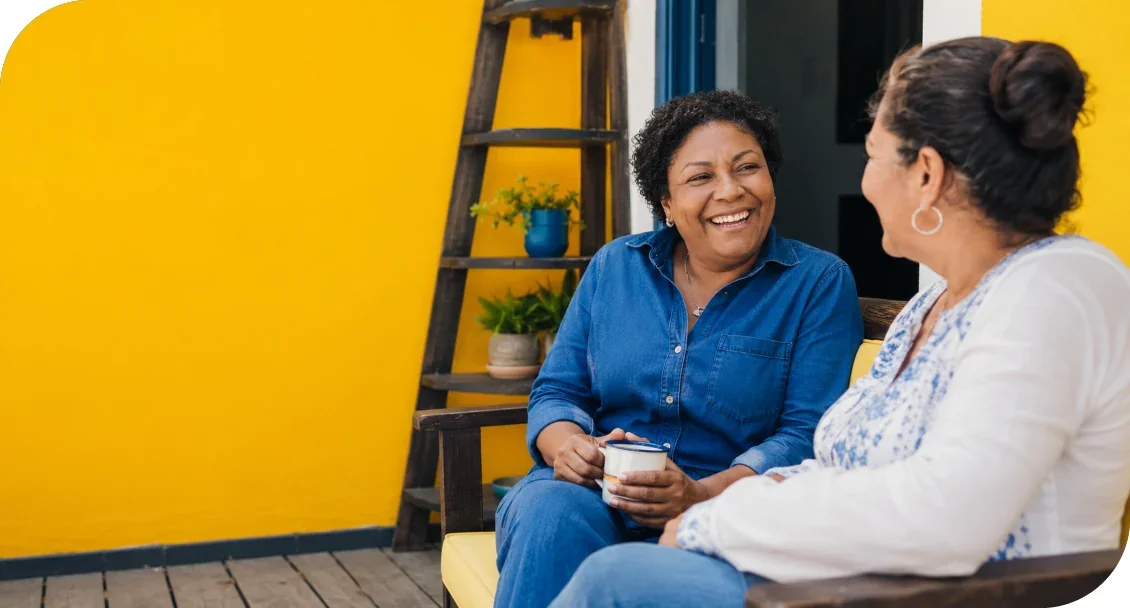 Two women smiling and talking together while seated on a porch.