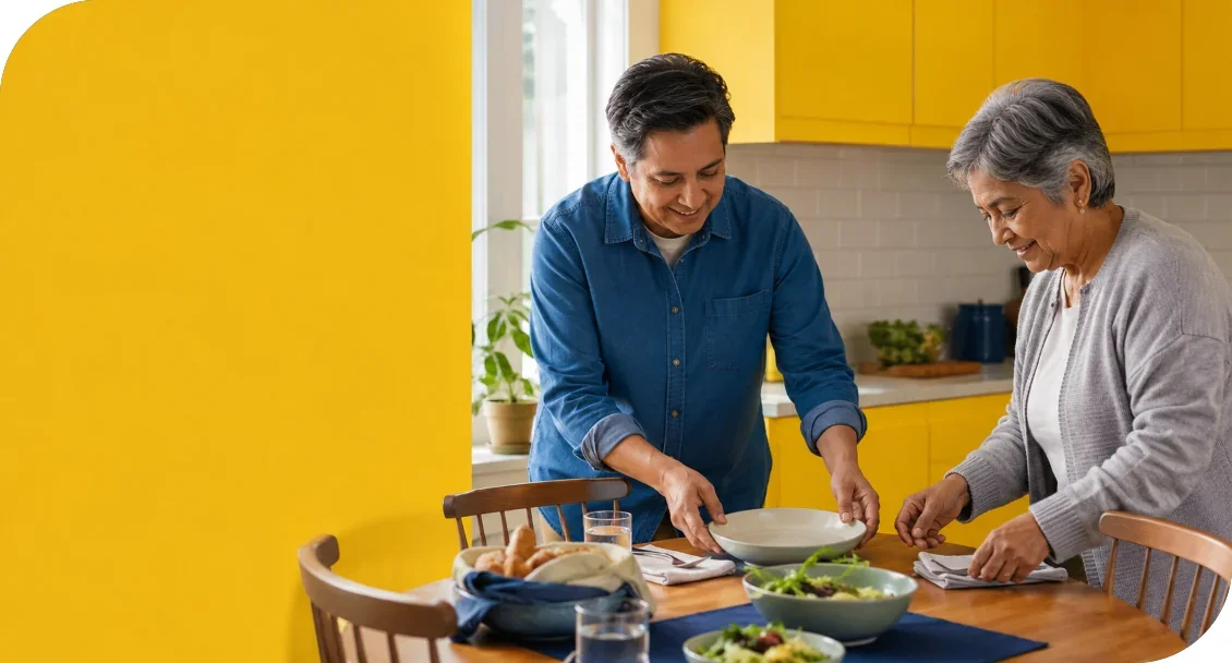 A man and an older woman preparing a meal together at a kitchen table.