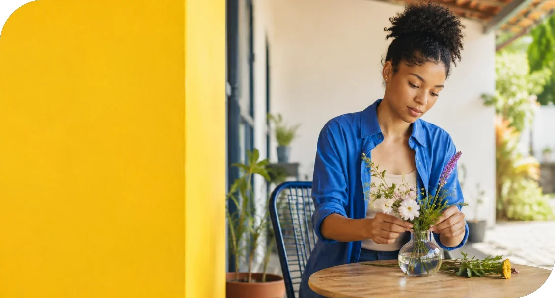 A woman arranging flowers in a vase at an outdoor table.