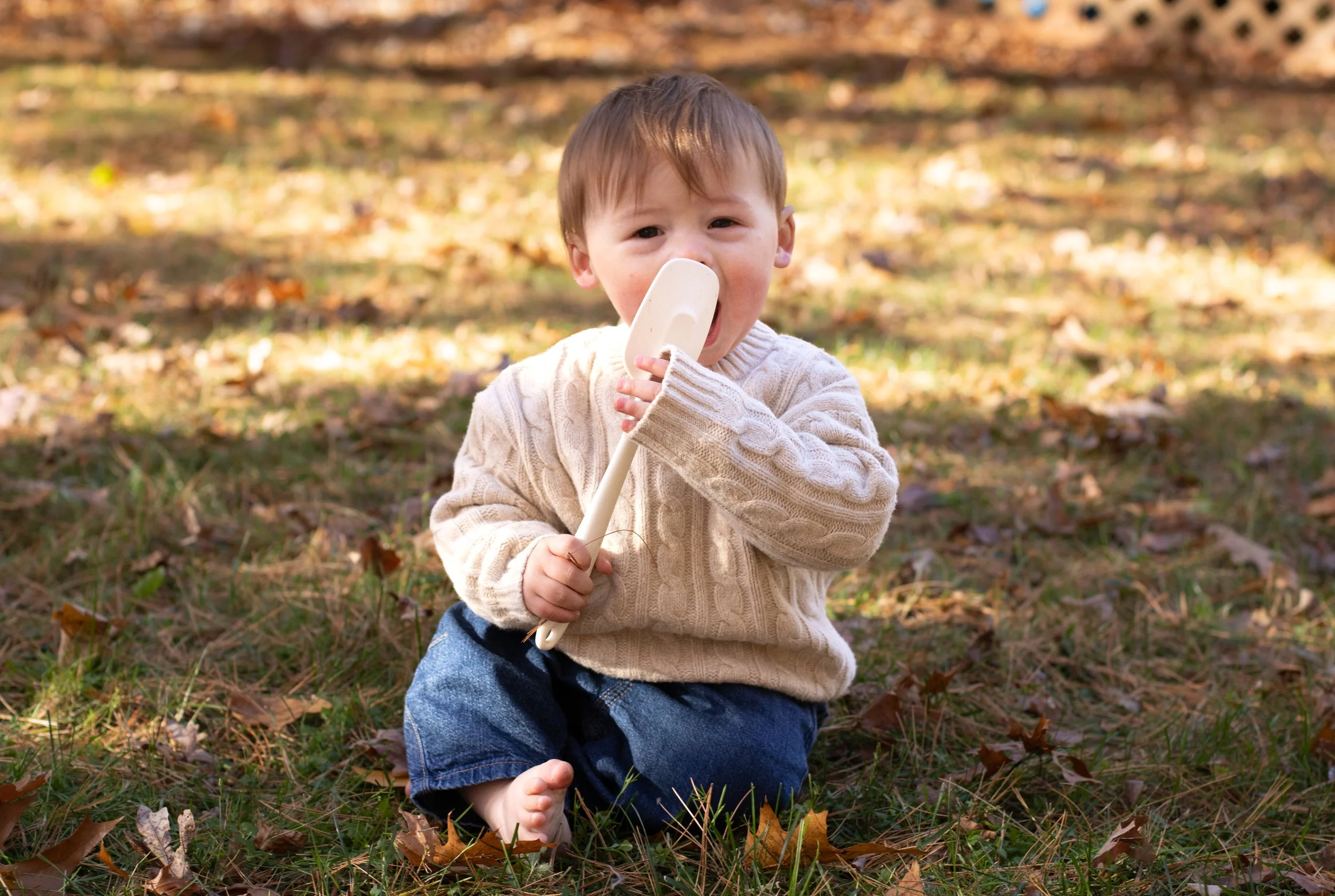 Baby sitting on autumn leaves holding a wooden toy during a fall family photography session by Boston photographer Sasha Parfenova.