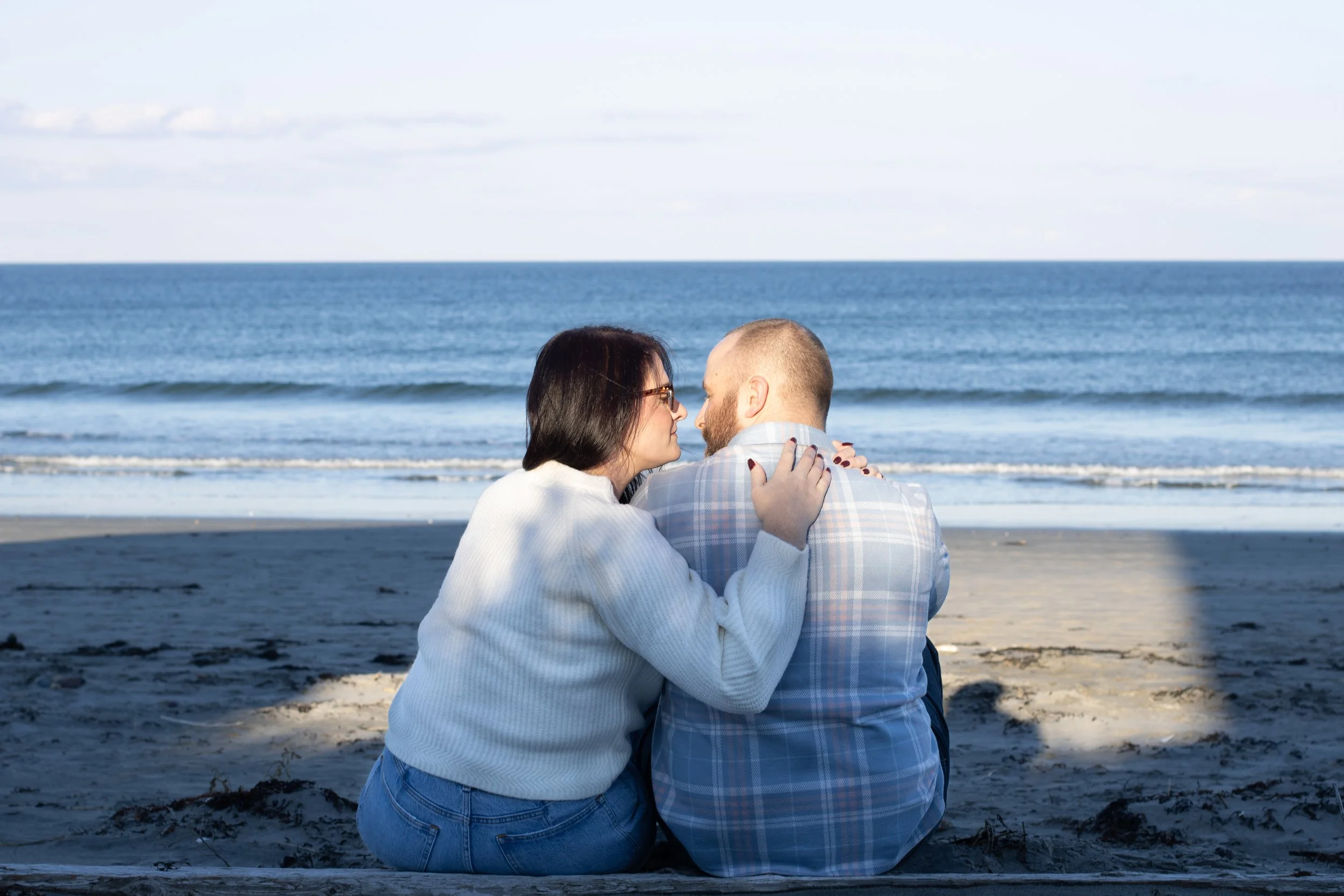 Couple sitting on the beach at sunset, sharing a kiss during a couples photography session by Boston photographer Sasha Parfenova.