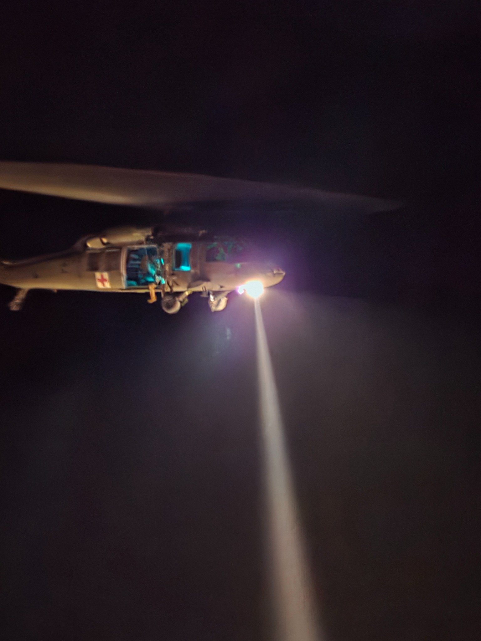 Helicopter hovering at night with its searchlight illuminating the mountain