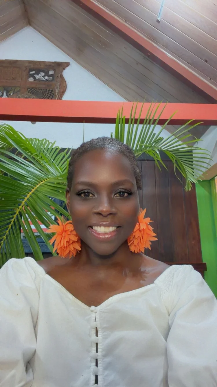 Merle-Tracey Galloway smiling, wearing a white top and orange flower earrings