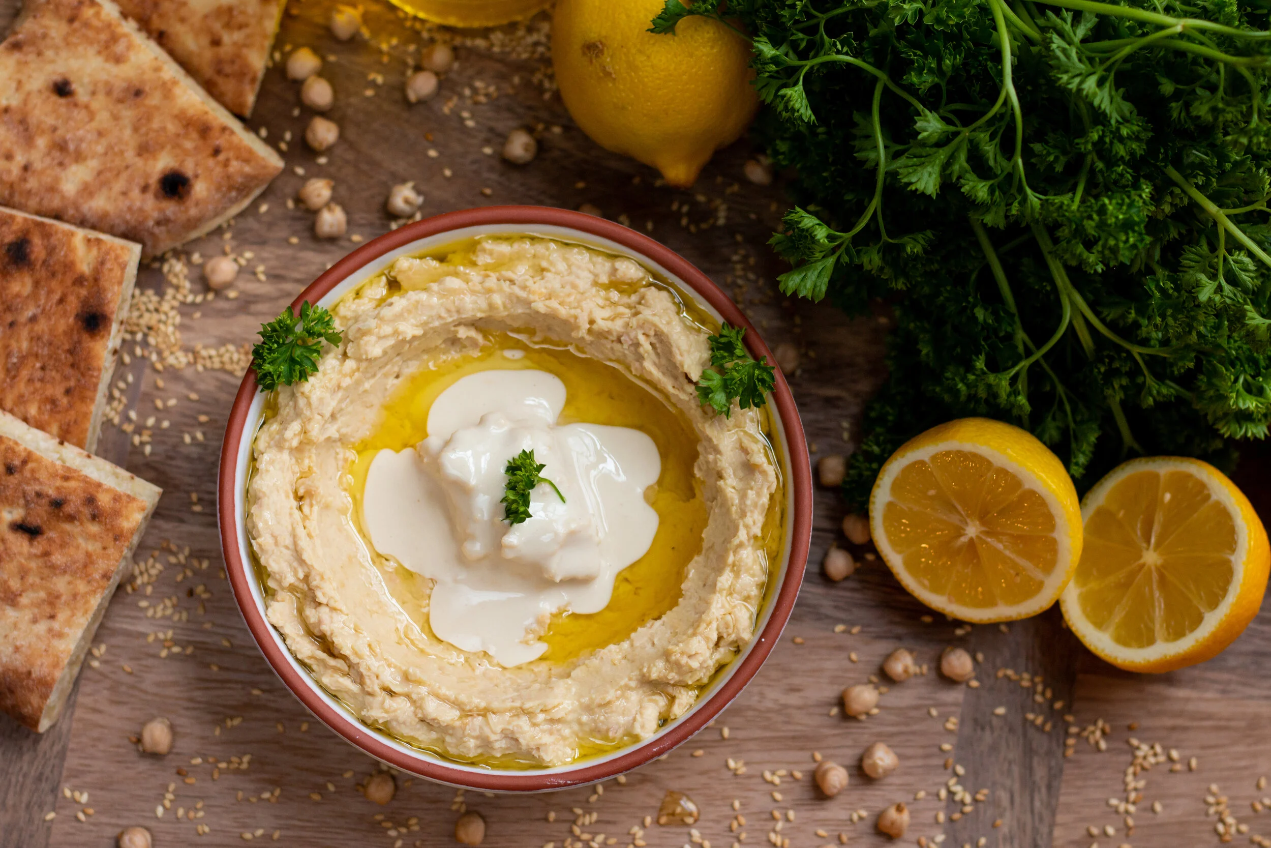 Overhead view of a Mediterranean spread with bowls of hummus, pita bread, and fresh vegetables on a rustic table.