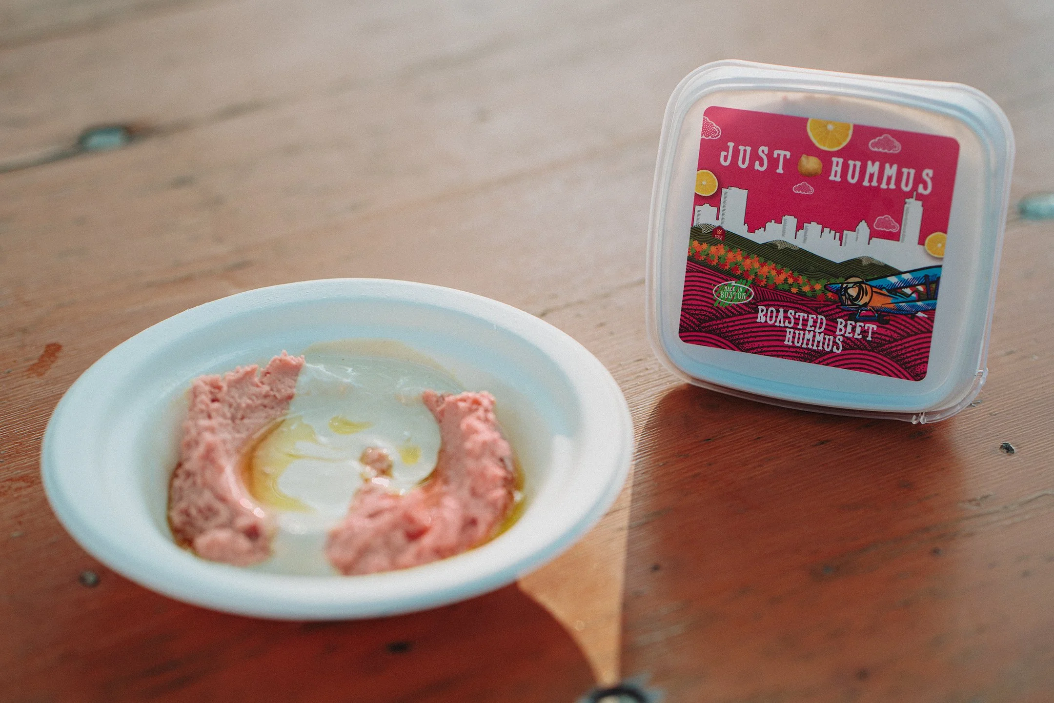 Roasted Beet Just Hummus packaging shown next to a bowl of Just Hummus topped with tahini dressing and olive oil