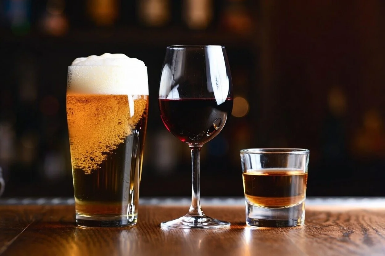 A beer, a glass of red wine and a whiskey pour side by side on a bar top