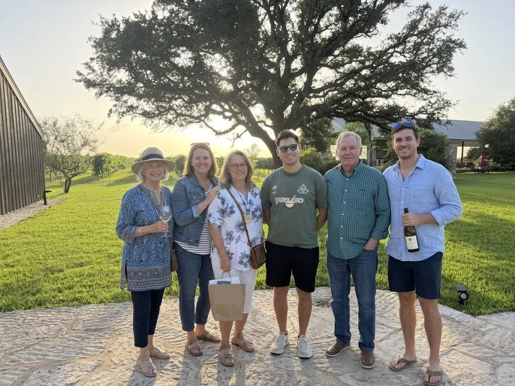 A Winding Road group raising glasses on a Fredericksburg winery lawn at golden hour