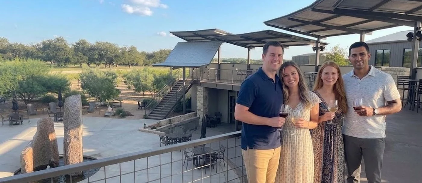 Two couples with wine on a winery terrace overlooking the Hill Country at golden hour
