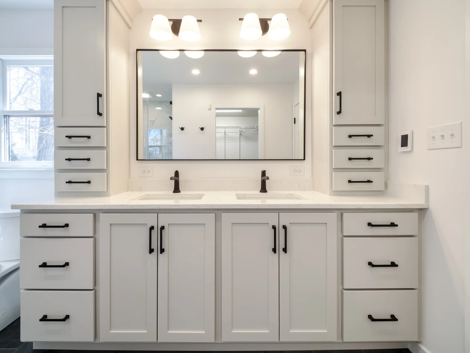 Double vanity in cream painted cabinetry with matte black hardware, a quartz top with two undermount sinks, tall linen towers on both sides and a large framed mirror