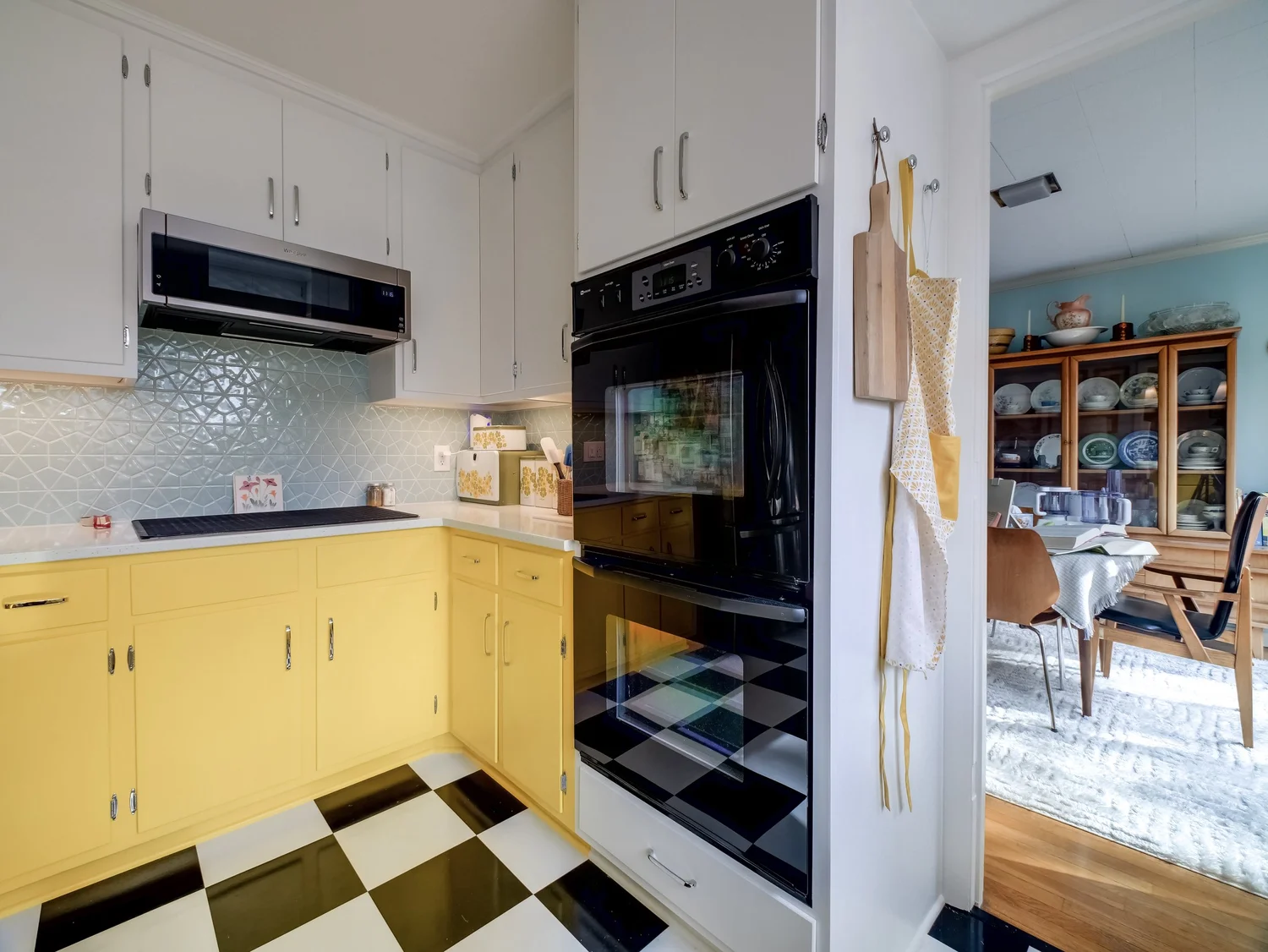 Two-tone kitchen with yellow lower cabinets, white upper cabinets, a pale blue geometric tile backsplash, and a black and white checkerboard floor