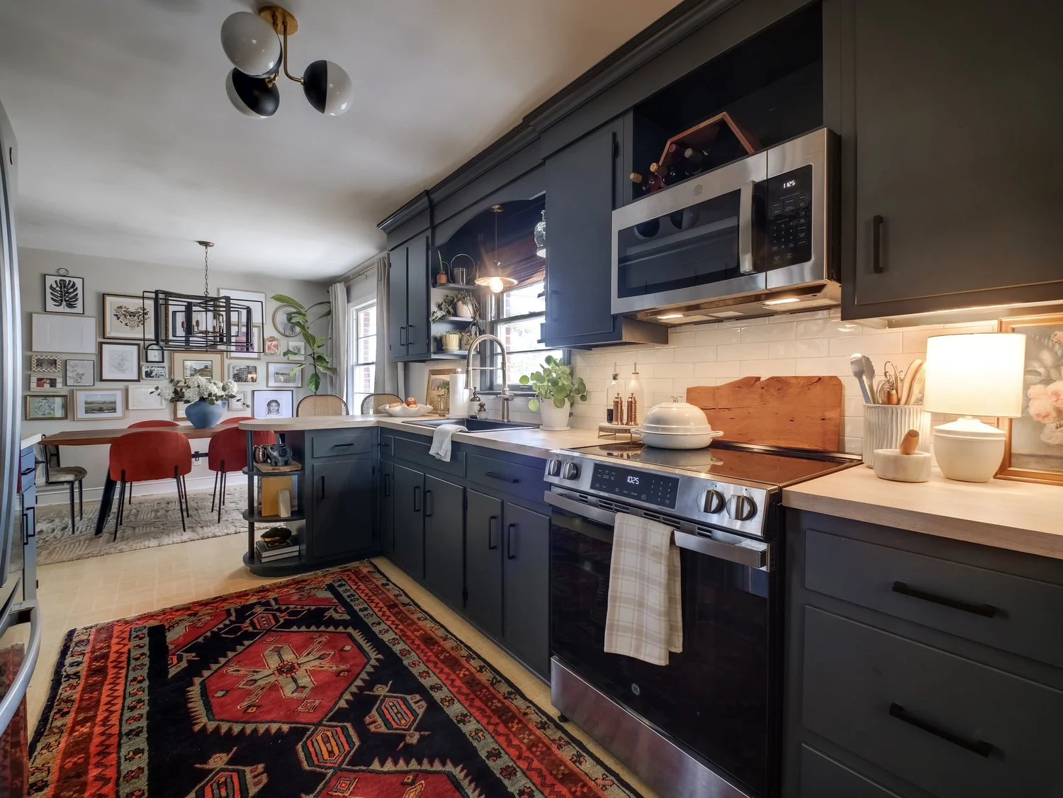 Charcoal blue kitchen cabinets with light butcher block counters, white subway tile, and open peninsula shelving looking through to the dining room