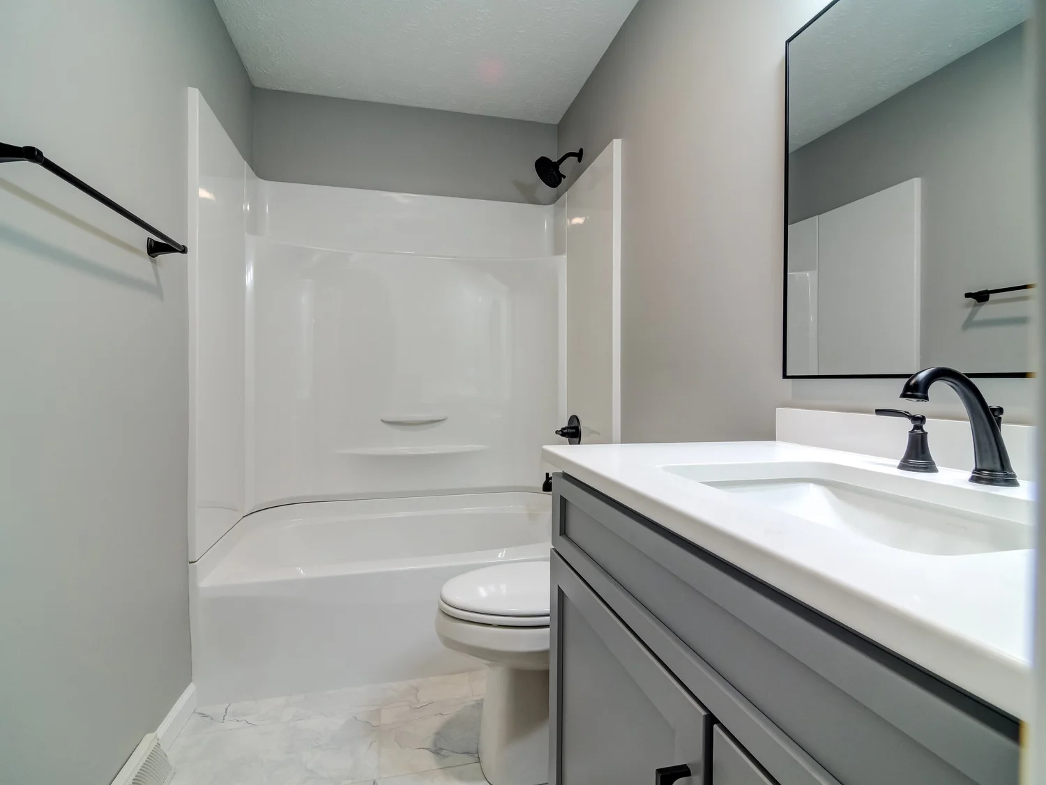 Hall bathroom with a white tub and shower surround, a gray vanity with a white quartz top, matte black fixtures and a marble-look tile floor