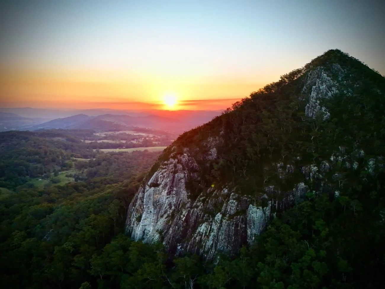 Aerial view of the sun setting over a mountain and valley