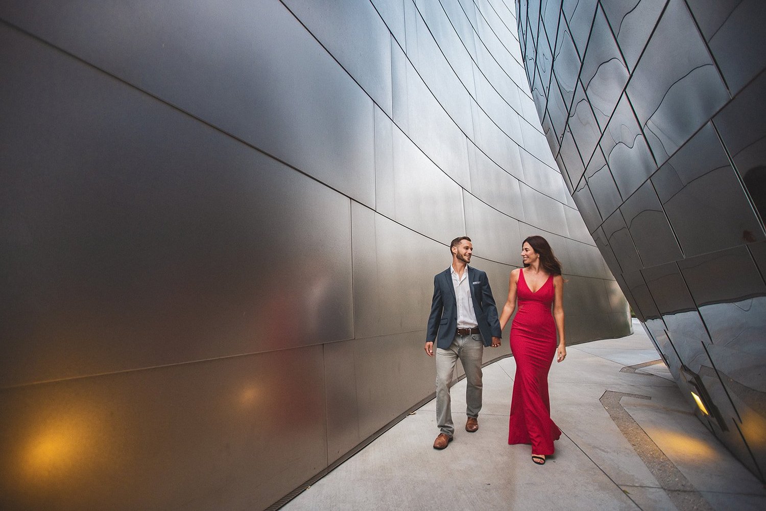 Couple walking between the curved stainless steel walls of Walt Disney Concert Hall, the bride in a red gown