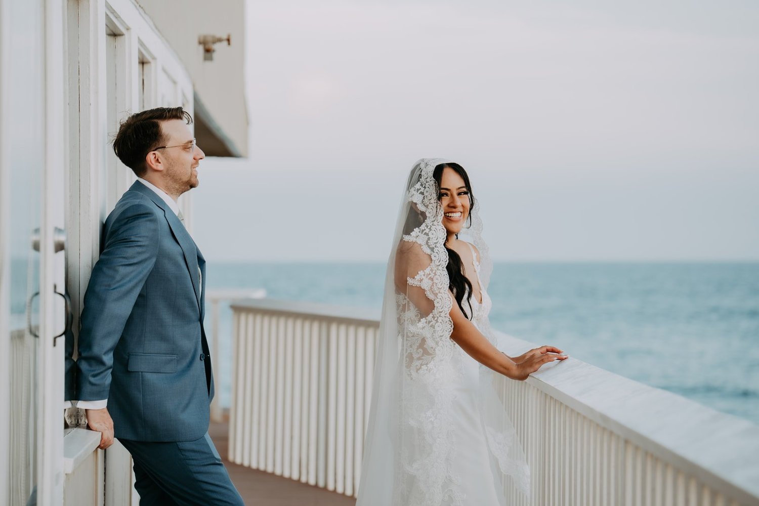 Groom leaning on the white oceanfront railing while the bride looks out to sea at Duke's Malibu