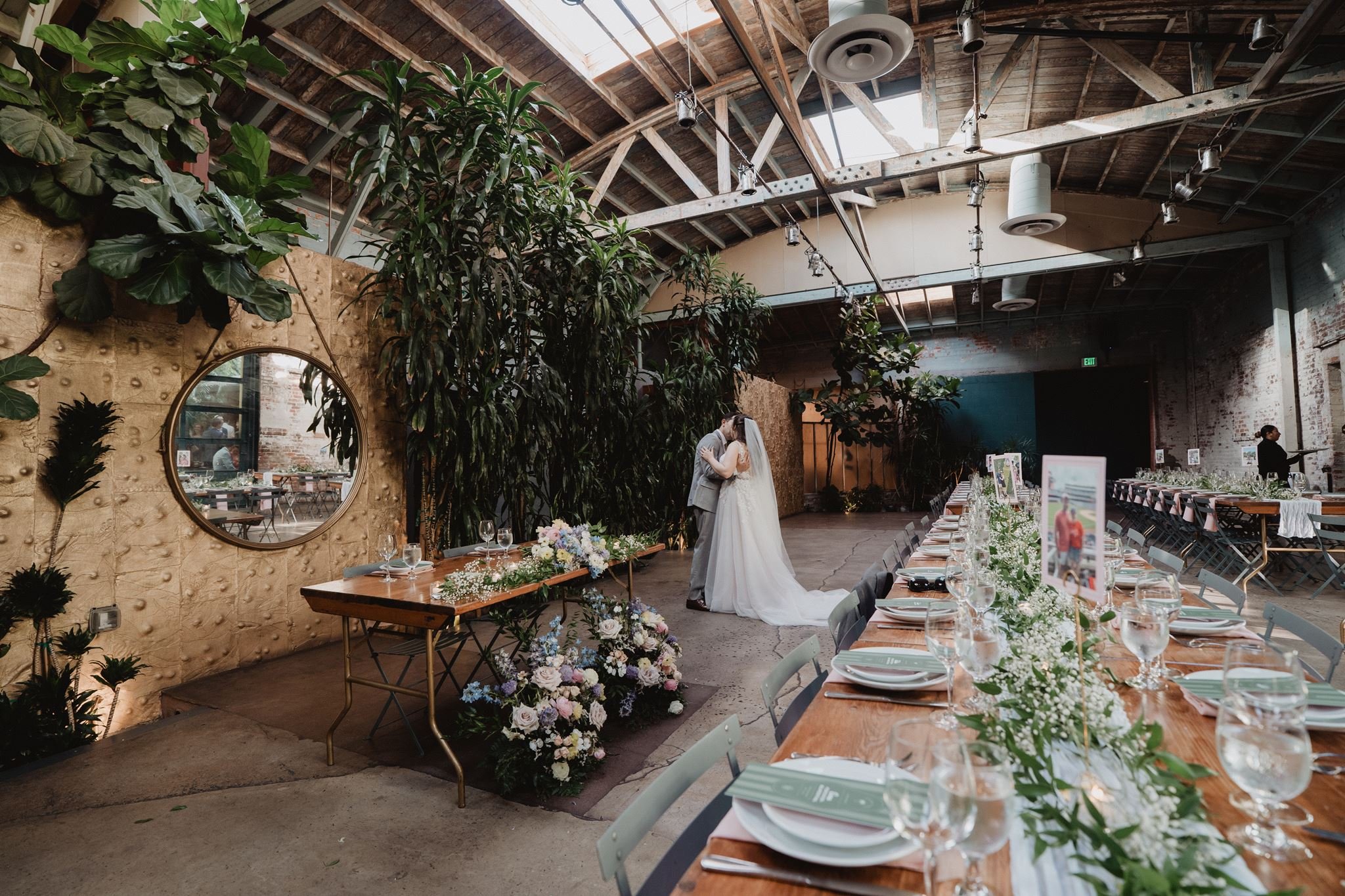 Long dinner tables with greenery under the wood trusses and skylights at Millwick in the Arts District
