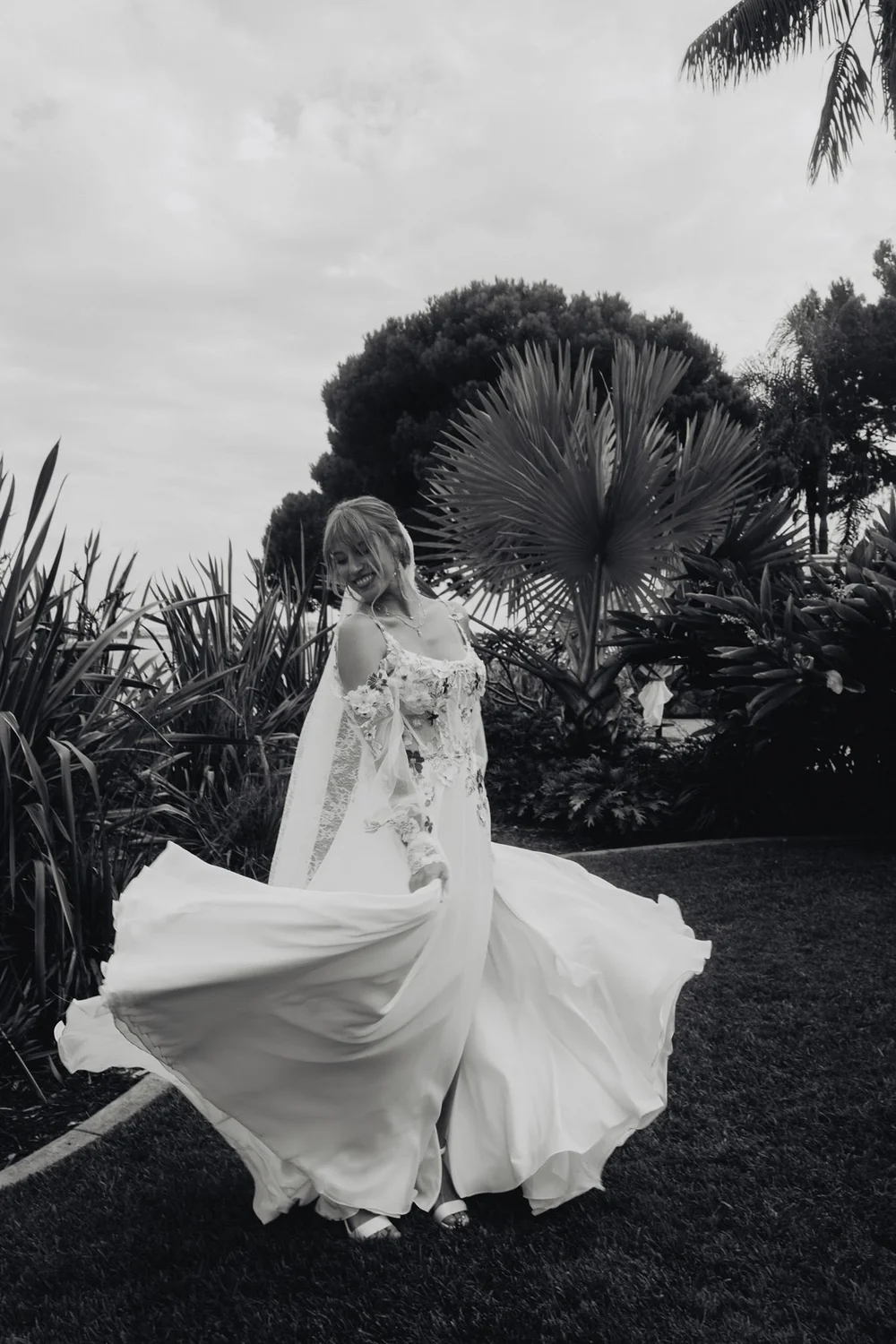 Black and white frame of the bride turning in her gown among the tropical planting at Bali Hai on Shelter Island