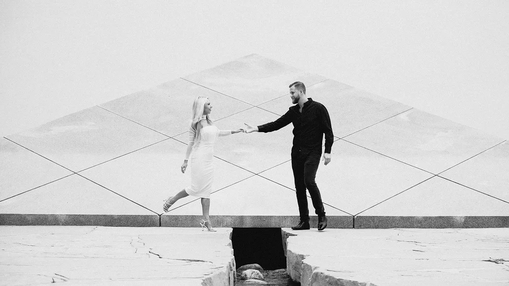 Black and white photograph of a couple reaching for each other across the stone plaza at the Noguchi Garden