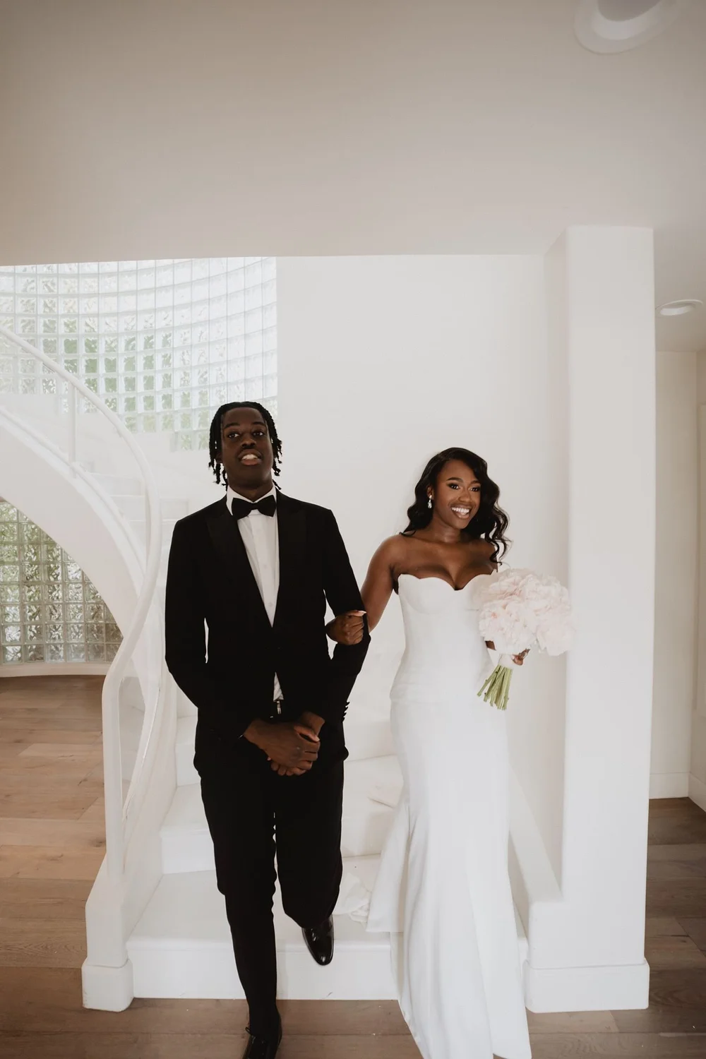 Bride in a plain strapless crepe sheath gown entering a bright modern space with her husband
