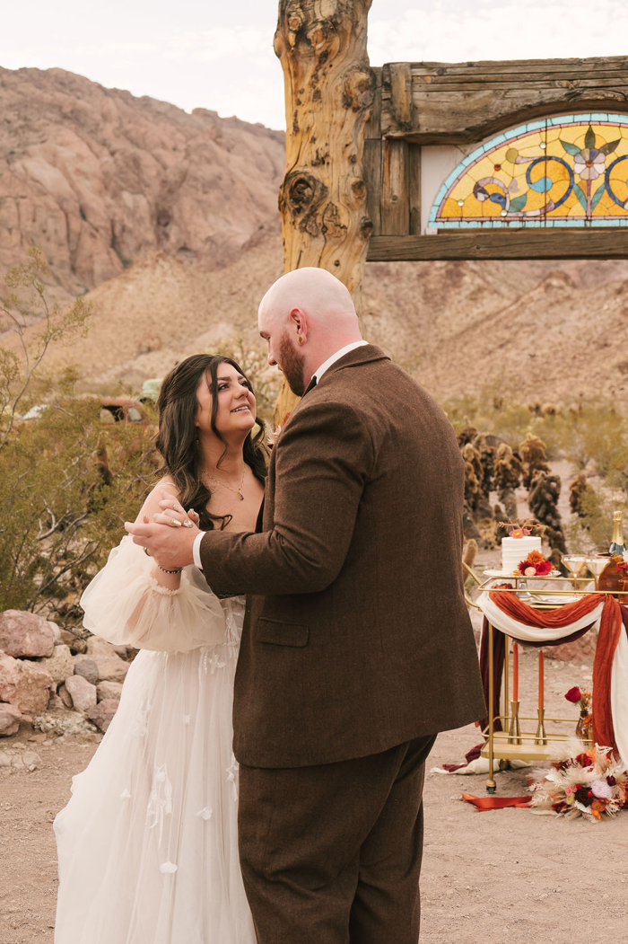 Bride in a tulle gown with sheer puff sleeves and groom in a brown tweed suit share a first dance beneath a stained-glass arch at Nelson Ghost Town.