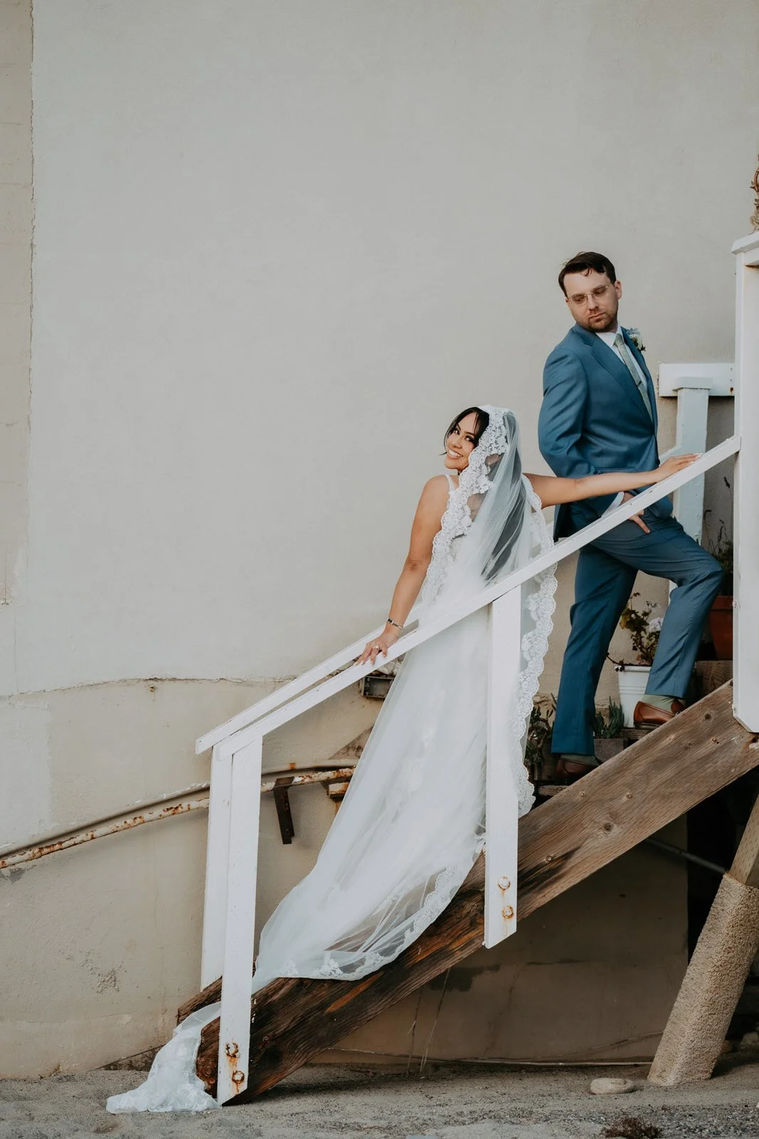 Couple climbing the white wooden beach stairs, veil trailing, at Duke's Malibu