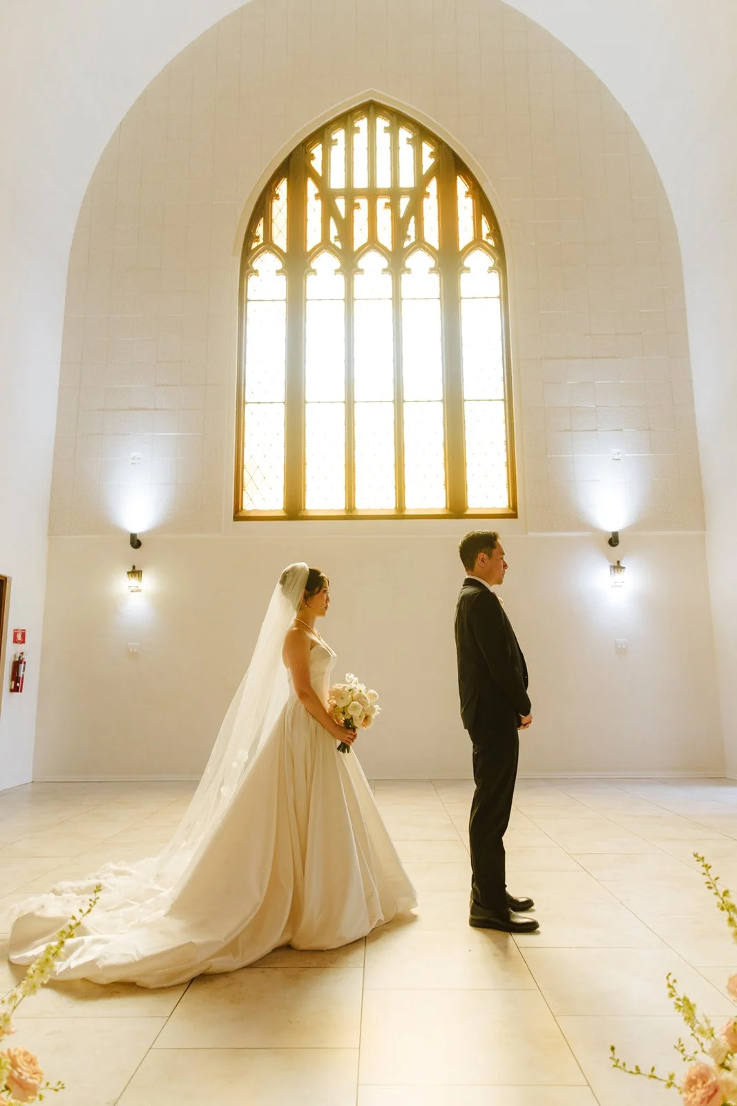 Bride and groom facing each other under the tall arched window at The Sanctuary