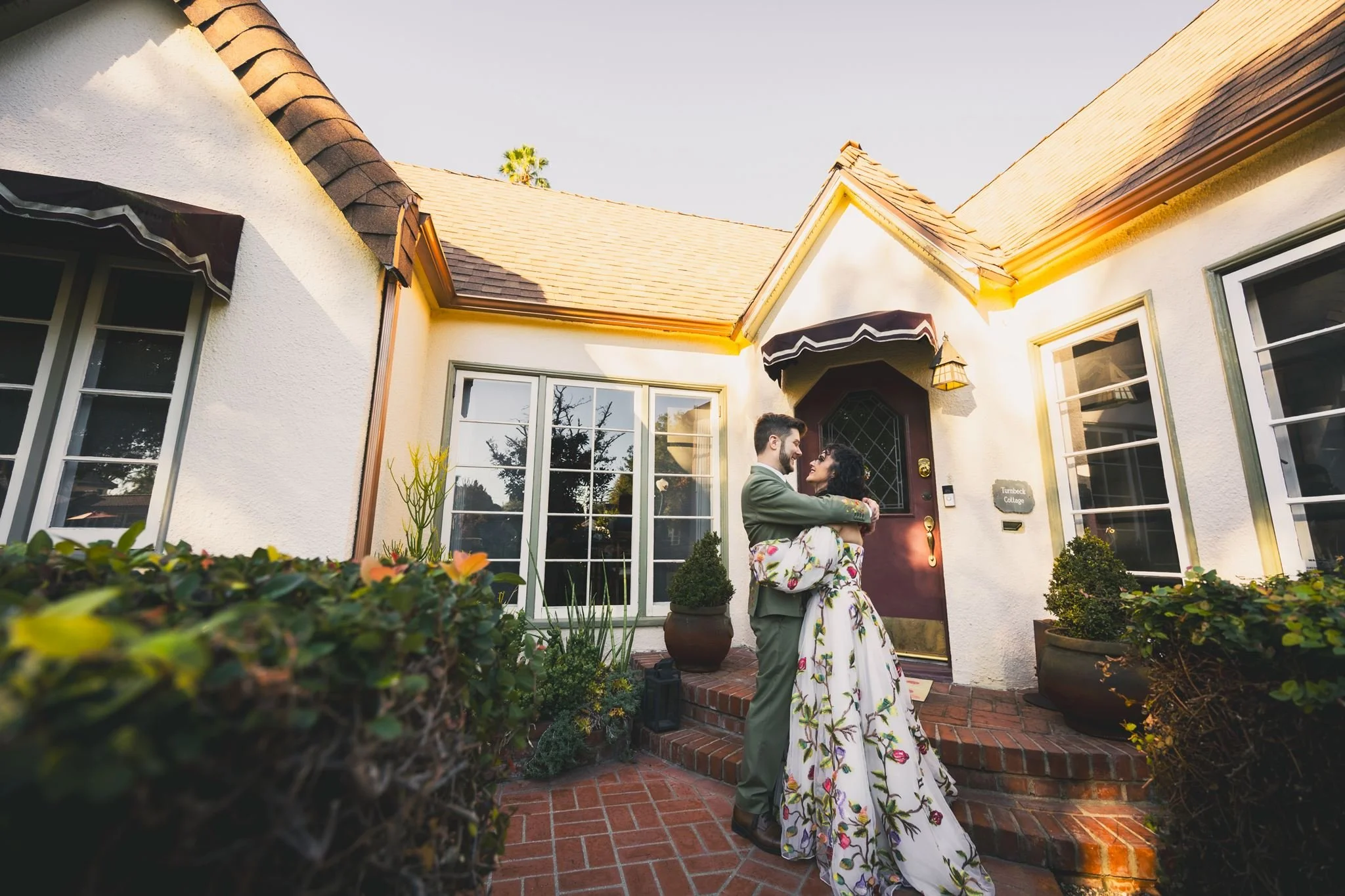 Couple at the brick steps of the white Spanish-style cottage at The Hacienda in Santa Ana, at dusk